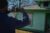 A figure takes a photo of a green house with his cellphone.
