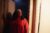 Charlotte Brown stands in a white doorframe in her home. She wears a red top and white headband and looks off-camera right.