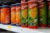 Cans of Kryzpo brand potato chips, labeled in Spanish, line a supermarket shelf. Black labels on each can warn they are "high in sodium" and "high in calories."