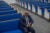 Pastor Allen Overton sits in a wooden pew with bright blue upholstery in his church. The pews cascade behind him in two rows.