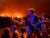 Two boys and other family members stand in the bed of a vehicle, watching wildfires in the distance in their neighborhood of Benito’s village, Spain. The sky glows orange and a blue glow is cast on the figures’ faces.