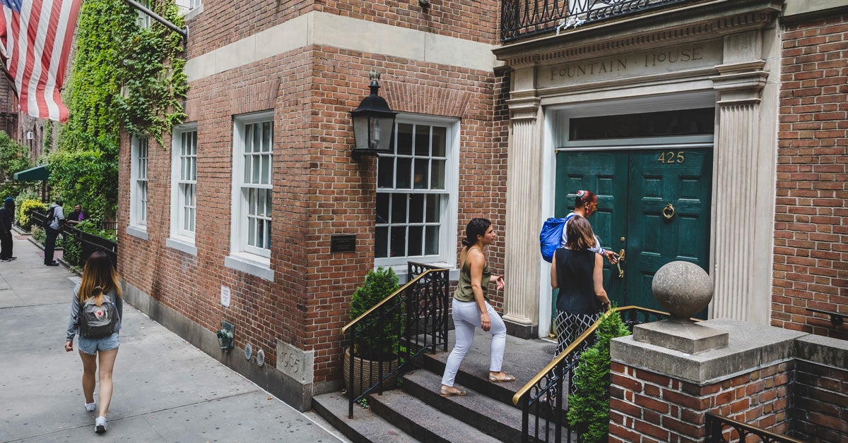 A historic New York City street with three people entering a brick building with the words “fountain house” above the entryway.
