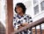 Anuoluwa Ishola leaning against a porch beam smiles broadly while looking off-camera.
