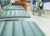 A man sits in a row of waiting room seats while nurses and wheel chairs move through a busy hallway at a hospital.