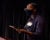 Kamilah Moore wears a black facemaks, bright white cat-eyed glasses and holds an ipad while speaking at a podium