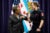 A female firefighter in dress fatigues bumps elbows with Mayor Lori Lightfoot at her graduation ceremony. The two stand in front of an American flag, a city of Chicago flag and two other flags.
