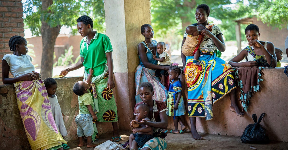 A group of African women and their children wait on a balcony.