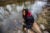 Marcel Simmons squats on some rocks near the edge of the Flint River. He stares somberly up at the camera.