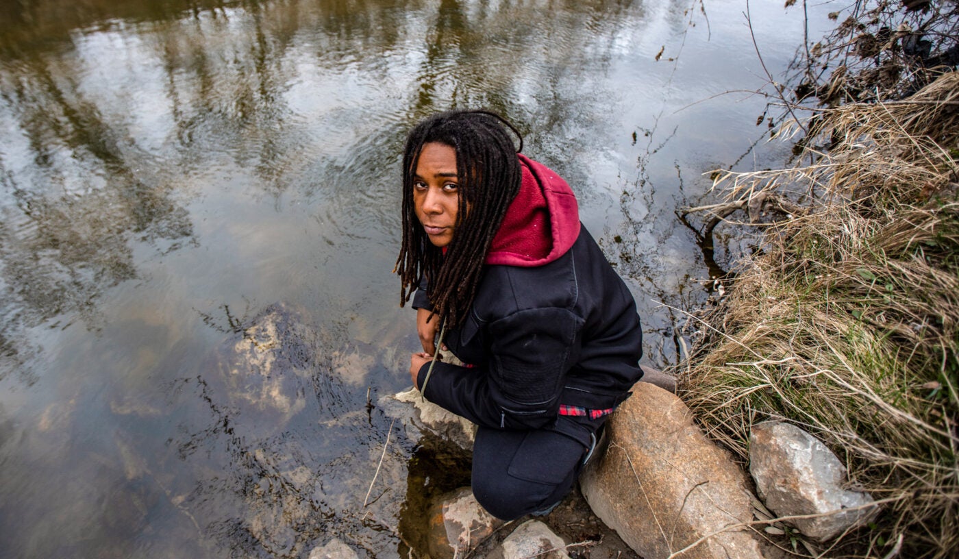 Marcel Simmons squats on some rocks near the edge of the Flint River. He stares somberly up at the camera.