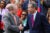 Phil Berger, Republican Senate majority leader, wearing a grey suit and orange tie, shakes hands with Gov. Roy Cooper, wearing a blue suit with a pink and blue striped tie. They are in front of a crowd of clapping black and white of North Carolinas.
