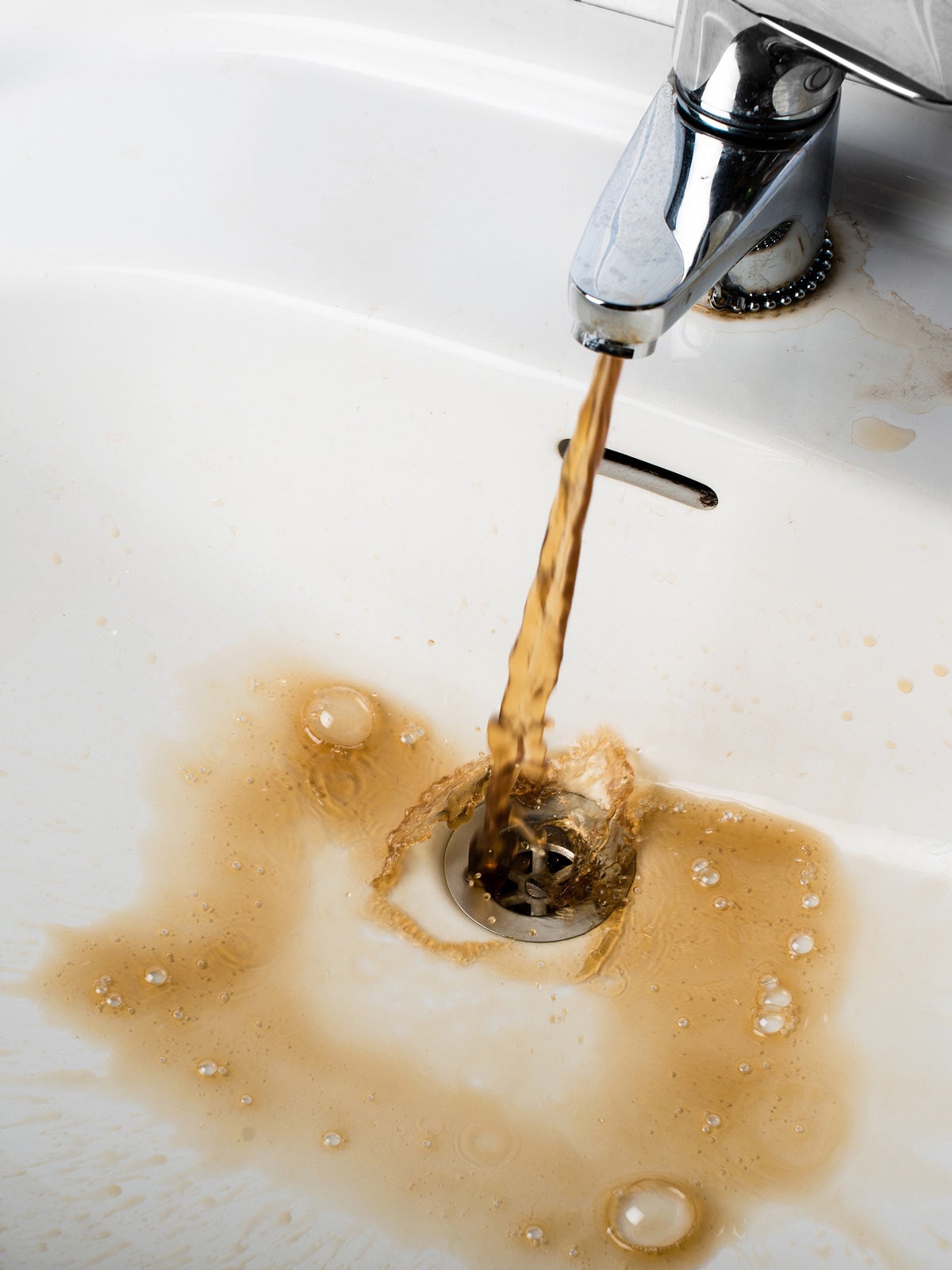 A silver faucet dispenses brown, murky water into a white bathroom sink.