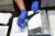 Two latex gloved hands hold a black comb as part of a displayed sexual assault evidence kit (rape kit). On the table are a bunch of swabs in a box, small envelopes and labels for clothes.