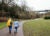 Two women wearing winter coats, jeans and bags, walk on a paved path in a nature park on a cloudy day.