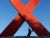 A giant AIDS red ribbon statue. A young silhouetted child pushes against one strand.