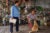A community outreach worker visits a prosthetics patient in his house in Kandal province, in southeastern Cambodia. The two smile at eaach other and a dog nestles near its owner.