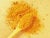 Bright yellow turmeric powder in a wooden spoon on a yellow background.