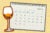 Photo illustration: A January calendar is marked with four check marks and one x for the first week of the month. In the foreground is a wine glass with orange liquid. The composition is on a yellow-speckled background.