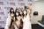 Six masked female students take a selfie in front of a photo backdrop with the Harvard Chan logo repeated.