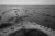 Black and white aerial photo: Parked RVs line a shoreline in Louisiana. In the water, there are narrow formations of land in diagonal patterns.