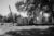 Black and white photo: A damage mobile home is spray painted with the words "water line" in a field in Louisiana.