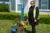 Cindi Enamorad, Olivares' sister, stands beside a memorial for her brother outside his Los Angeles home. There are flowers in a pot and a blue painted sign that says, “in loving memorie / Raymond Olivares.” Enamorad is wearing a traffic safety vest.