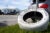 A tire, that has been painted white, is chained to a metal post, as a memorial for Raymond Olivares. The tire has hearts painted on it, and text that says, “5/21/95 / Raymond / 2/19/23 / Always & Forever!”