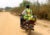 A man rides a motorcycle in rural Nigera. He wears a neon yellow vest with the words "COVID-19 vaccine is safe. Get vaccinated" and a Rotary logo.