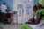 A mother holds her infant in her lap in a clinic room in a central Africa. A healthcare worker stands in the left corner writing notes with her back to the camera.